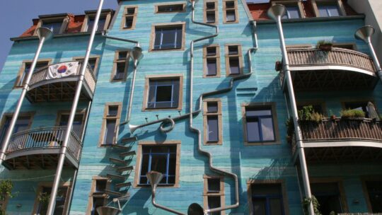 Zu sehen ist ein türkisfarbenes, künstlerisch aussehendes Haus